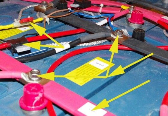 Yellow arrows point to areas of concern in this battery installation: uncovered terminals and fuses that may be substandard.