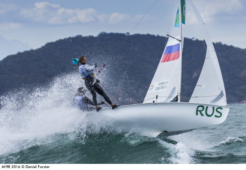 Eine olympische Zweimannjolle der 470er Klasse. Die Crew steht bei viel Wind im Trapez, um dem Boot Stabilität zu verleihen. Das Schwert unter dem Boot ist im Wellenkamm sichtbar. Foto: World Sailing/Daniel Forster