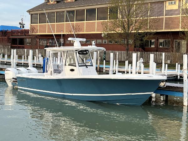 Regulator 34 2023 Regulator 34 boat docked in marina, blue hull, white cabin, waterfront building background.