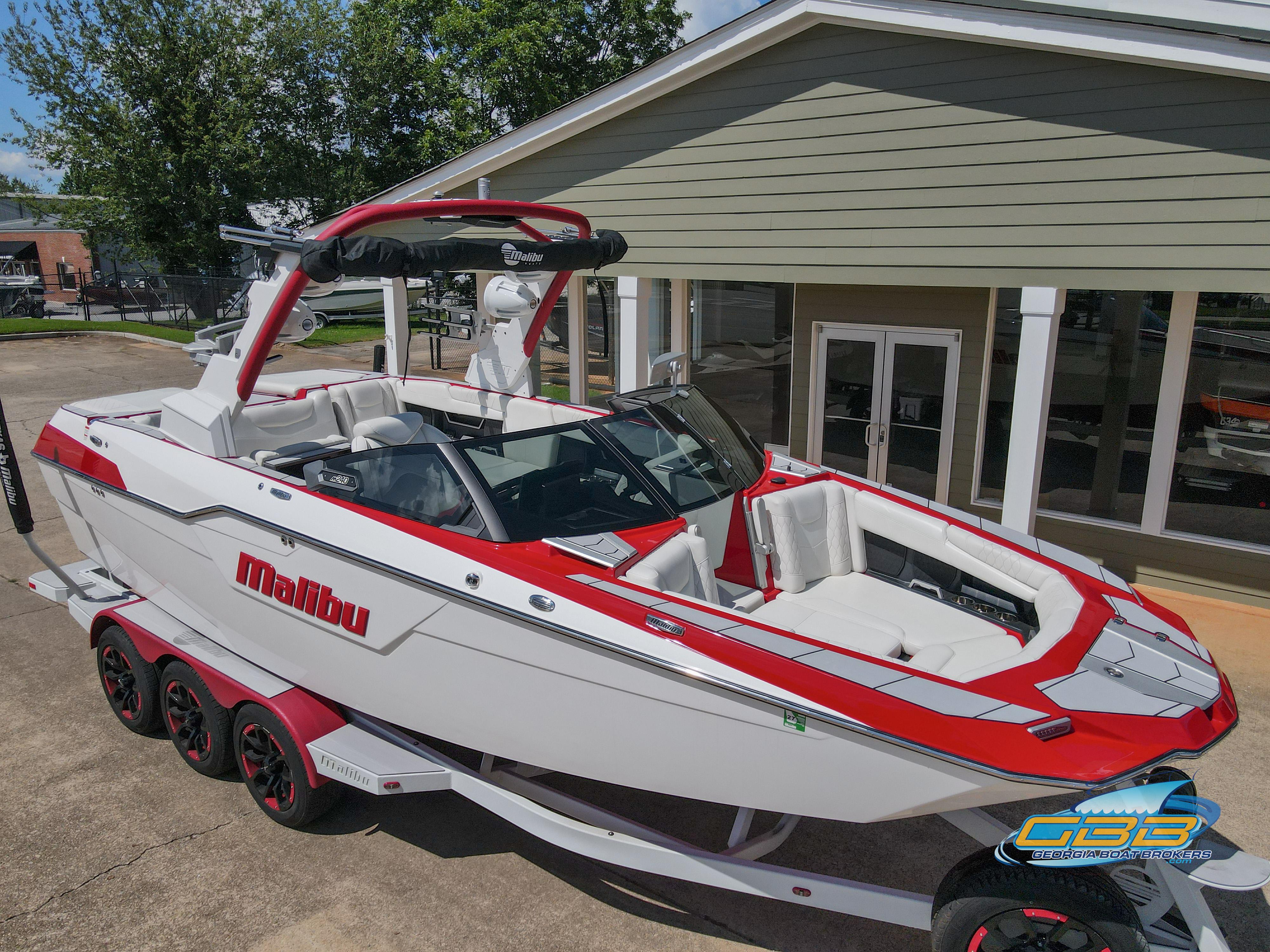 Malibu M240 2021 Malibu M240 boat with red and white design, parked on a trailer outside a building.