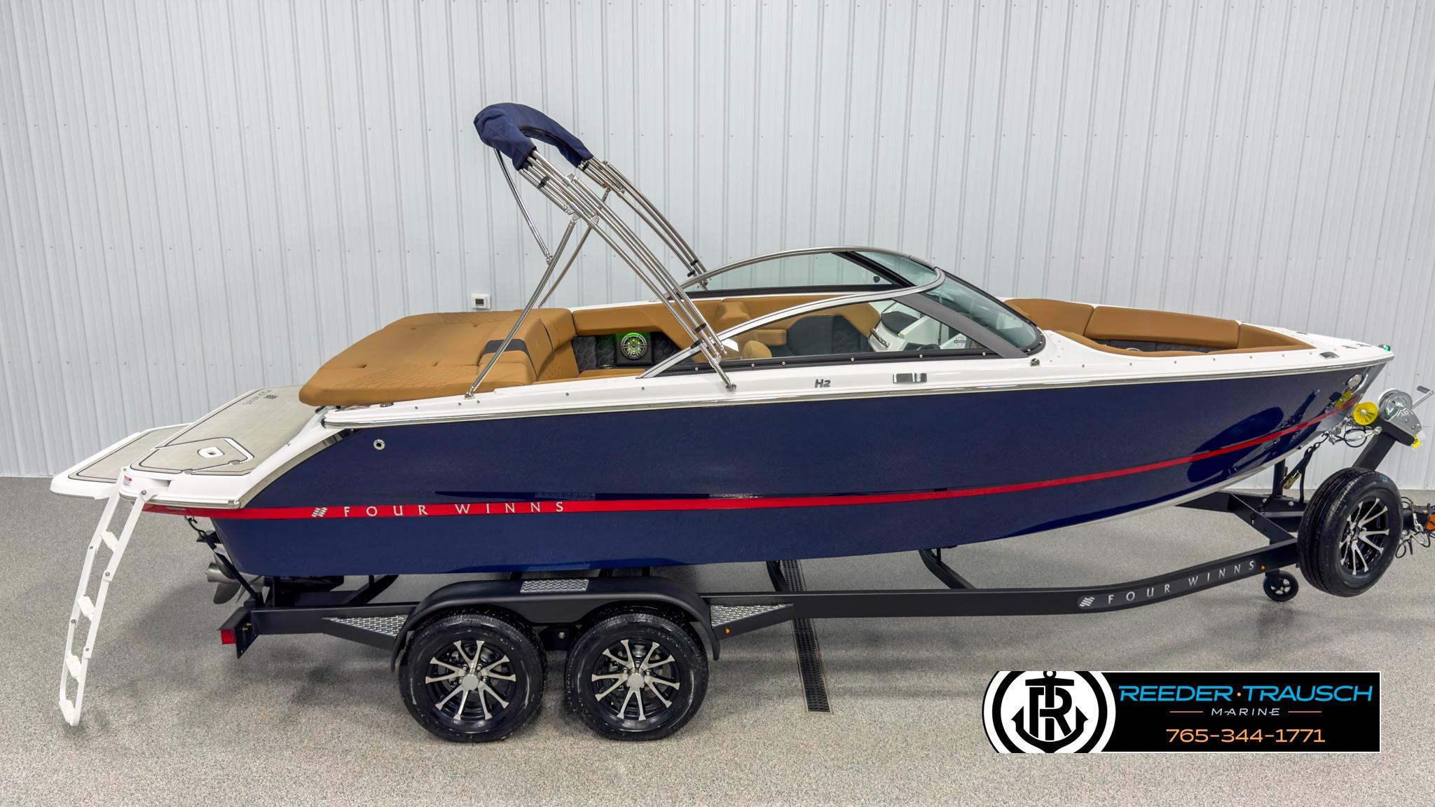 Four Winns H2 2025 Four Winns H2 boat on trailer, blue with tan interior, displayed indoors.