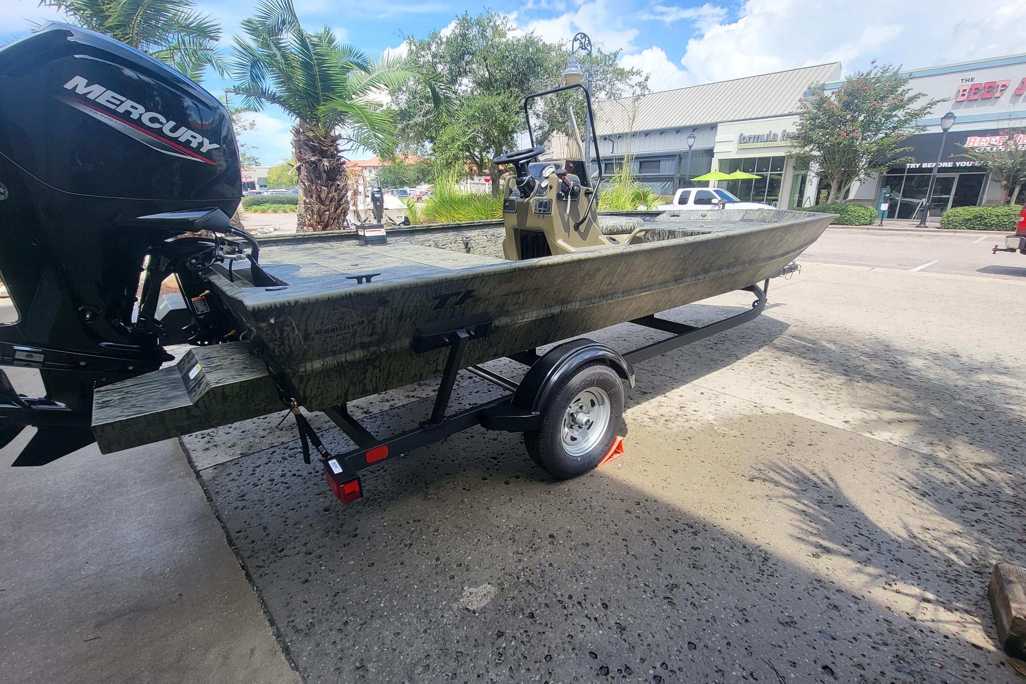 Tracker Grizzly 1860 CC 2026 Tracker Grizzly 1860 CC boat on trailer, parked outdoors near shops.