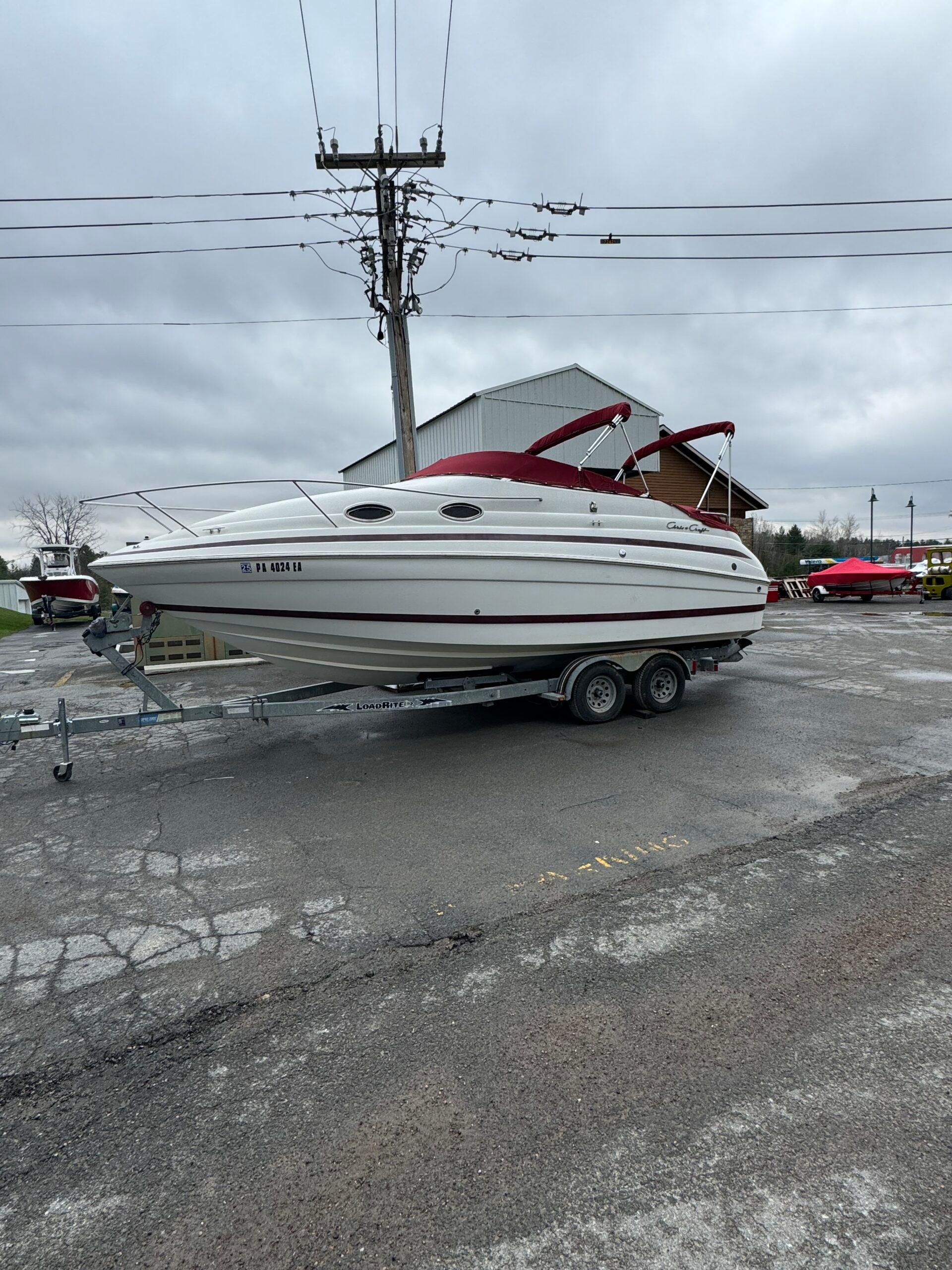 Chris-Craft 24 1999 Chris-Craft 24 boat on trailer, parked outdoors under cloudy sky.