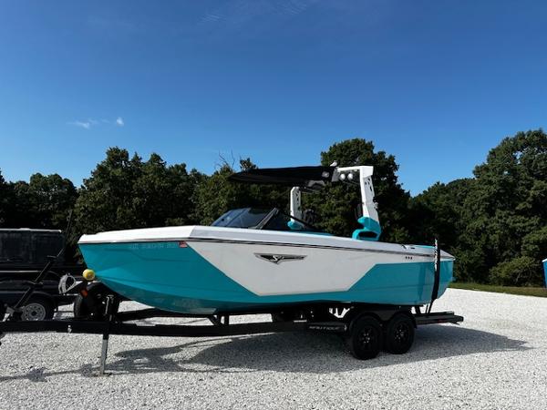Nautique S23 2022 Nautique S23 boat in turquoise and white on a trailer, parked outdoors.