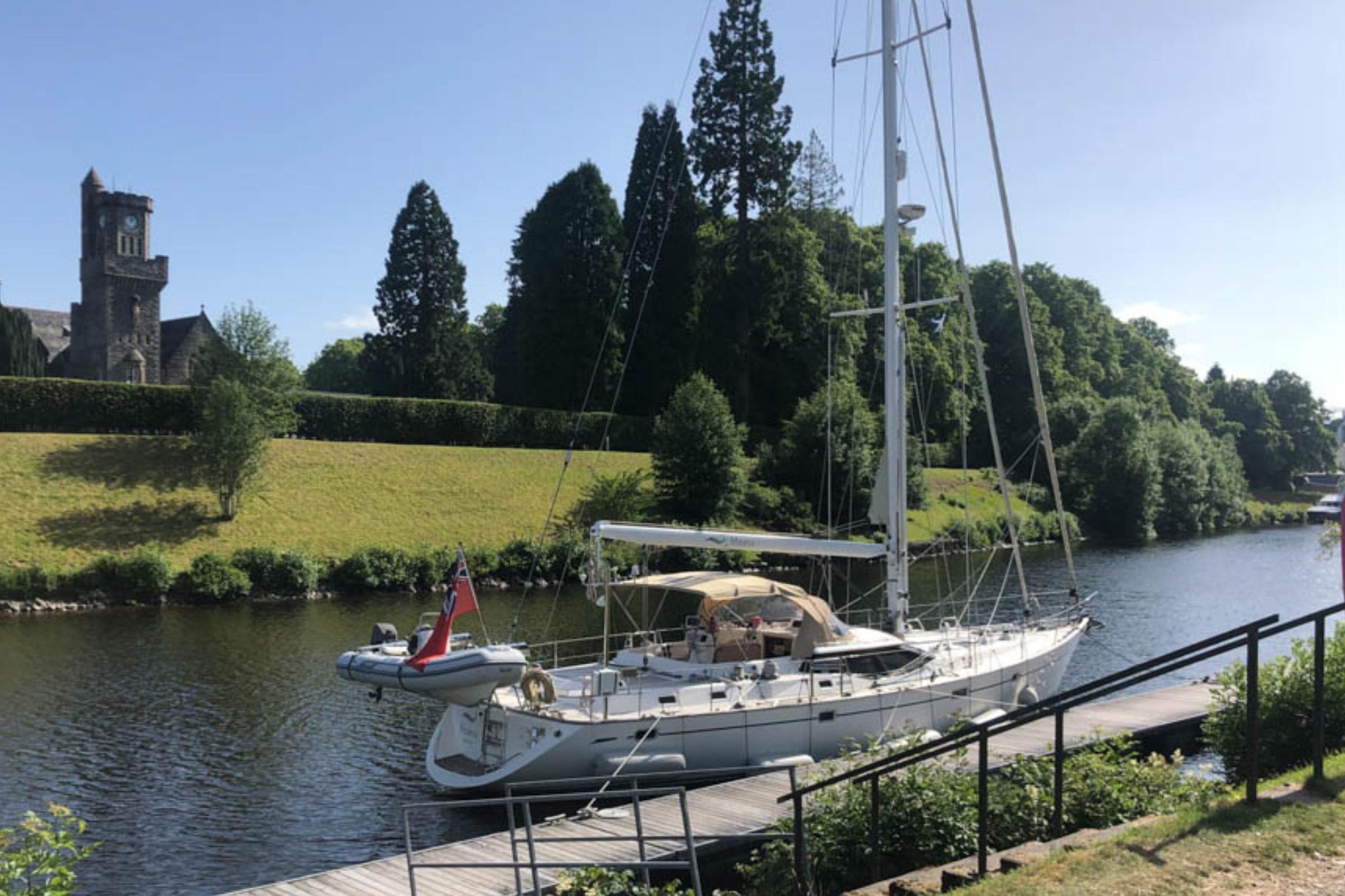Oyster 56 Sailing yacht Oyster 56 (2003) docked by a scenic riverside with lush greenery.