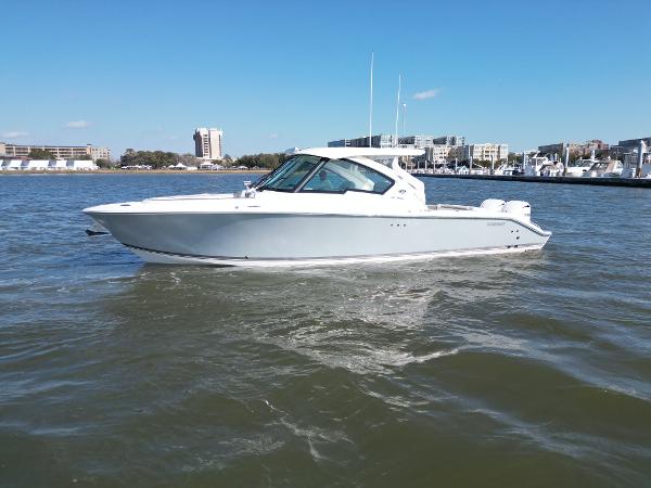 Pursuit DC 326 Dual Console 2023 Pursuit DC 326 Dual Console boat on calm water, cityscape background.