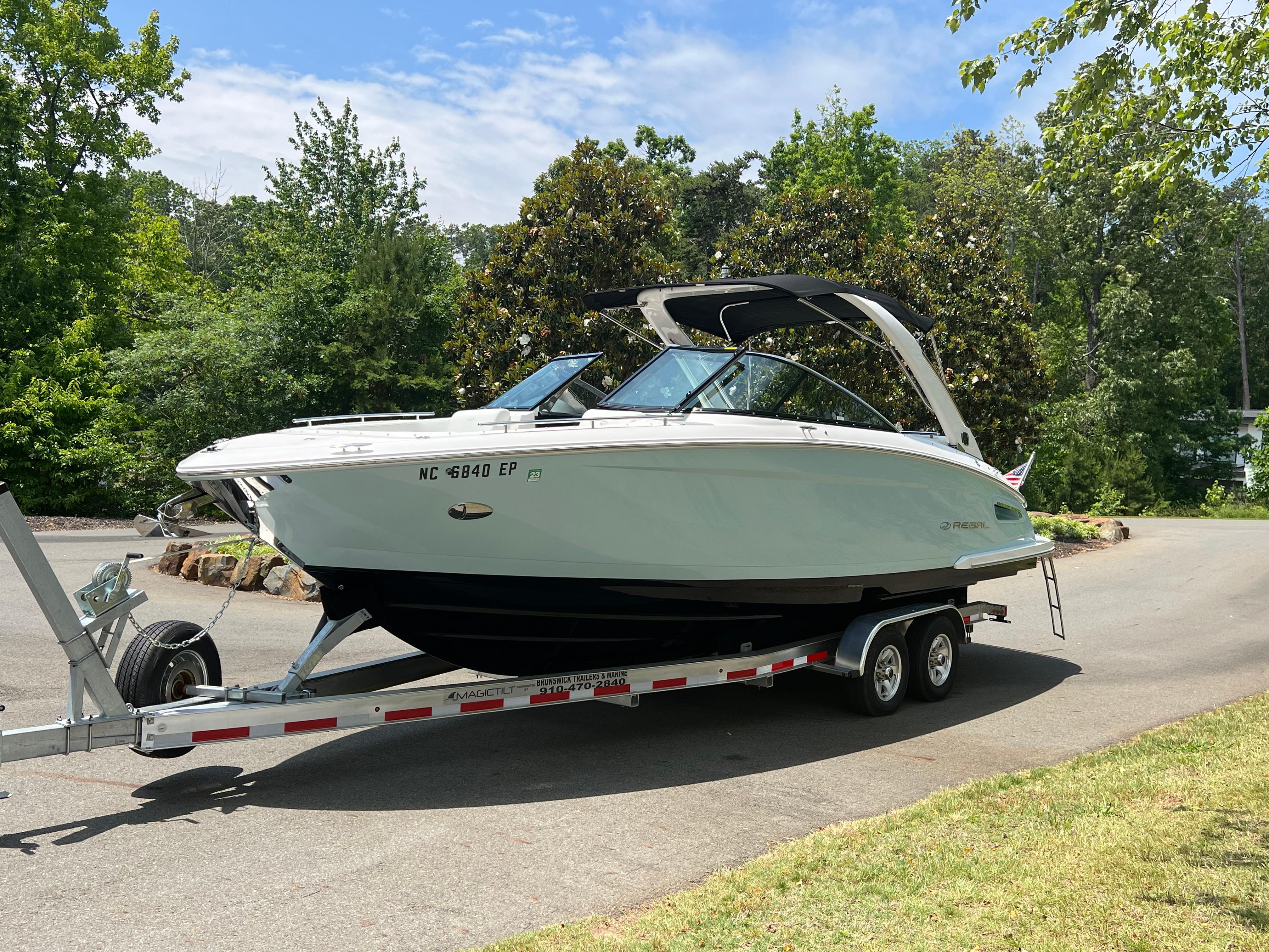 Regal 2800 Bowrider 2020 Regal 2800 Bowrider on trailer, parked on a sunny road with lush greenery.