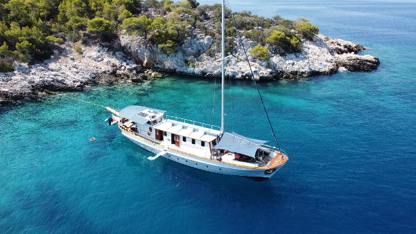 Custom Mavrikos Motor Sailer Custom 1979 Mavrikos Motor Sailer anchored near rocky coastline with lush greenery.