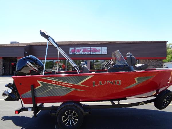 Lund 1675 Adventure SS 2024 Lund 1675 Adventure SS boat, red exterior, parked on trailer outside a building.
