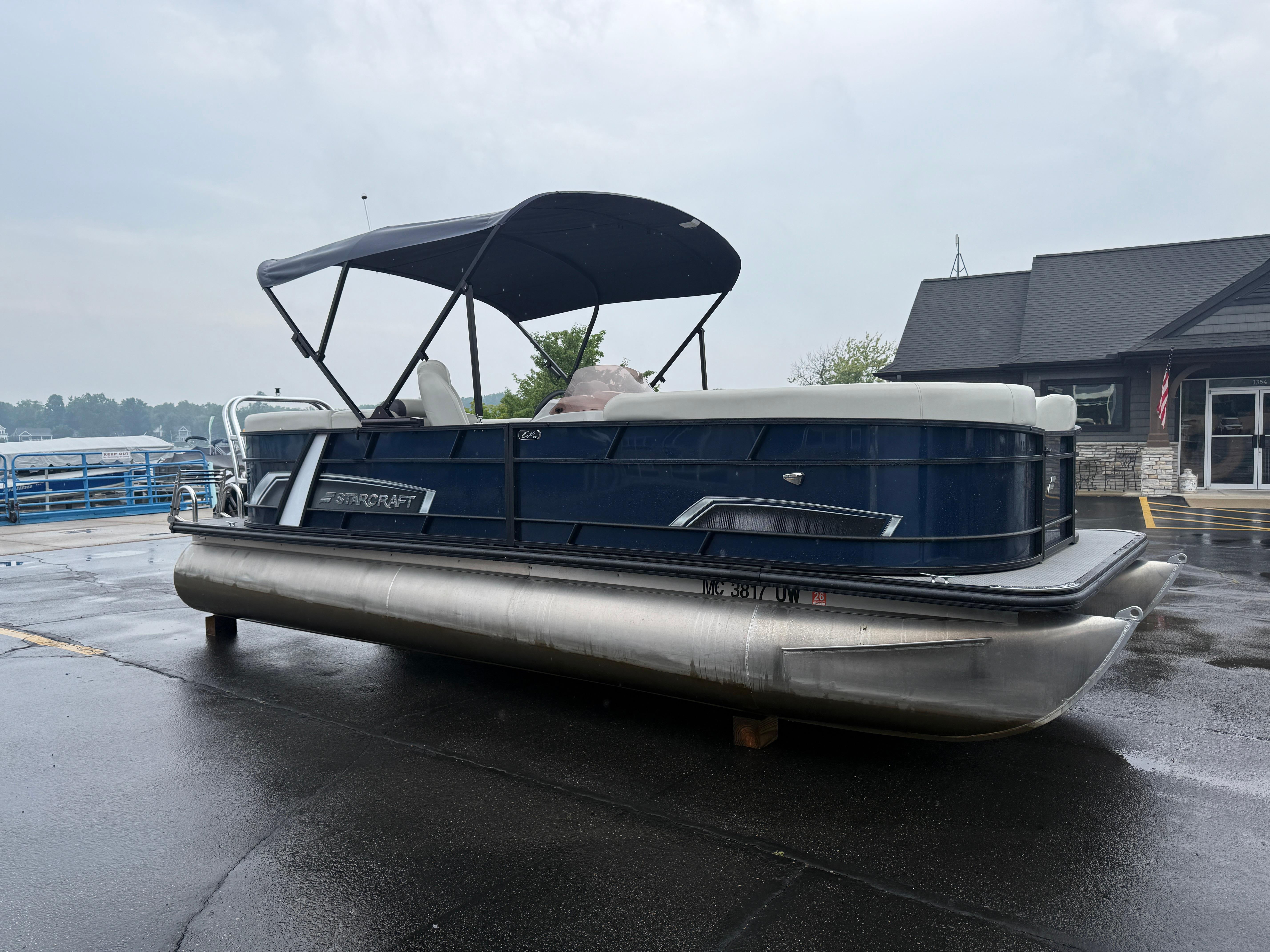 Starcraft EX22 2023 Starcraft EX22 pontoon boat with canopy on wet pavement near a building.