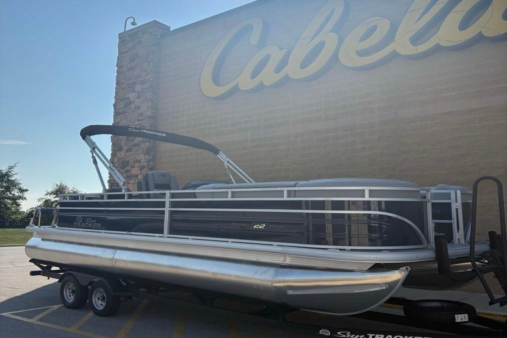 Sun Tracker SportFish 22 DLX 2026 Sun Tracker SportFish 22 DLX pontoon boat parked outside Cabela's store.