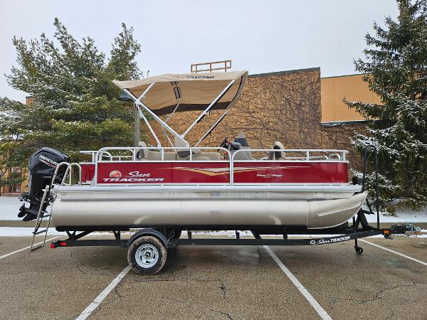 Sun Tracker Bass Buggy 18 DLX 2025 Sun Tracker Bass Buggy 18 DLX pontoon boat on trailer in parking lot.