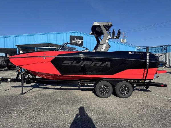 Supra SA 2025 Supra SA boat in red and black on a trailer, parked outside a blue building.