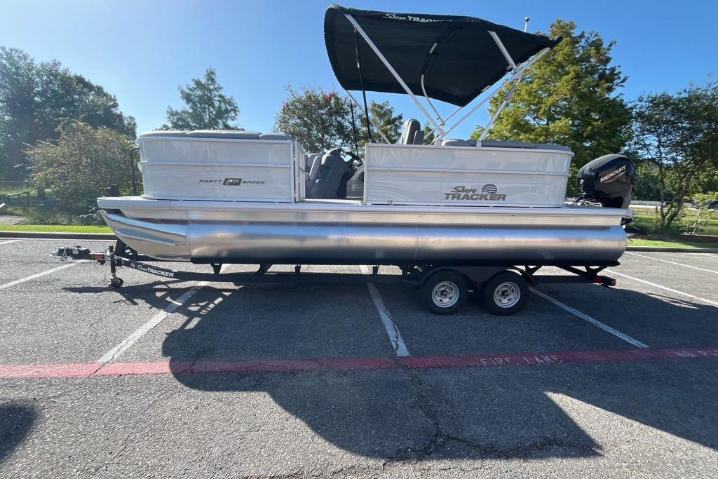 Sun Tracker Party Barge 22 DLX 2026 Sun Tracker Party Barge 22 DLX pontoon boat on trailer in parking lot.