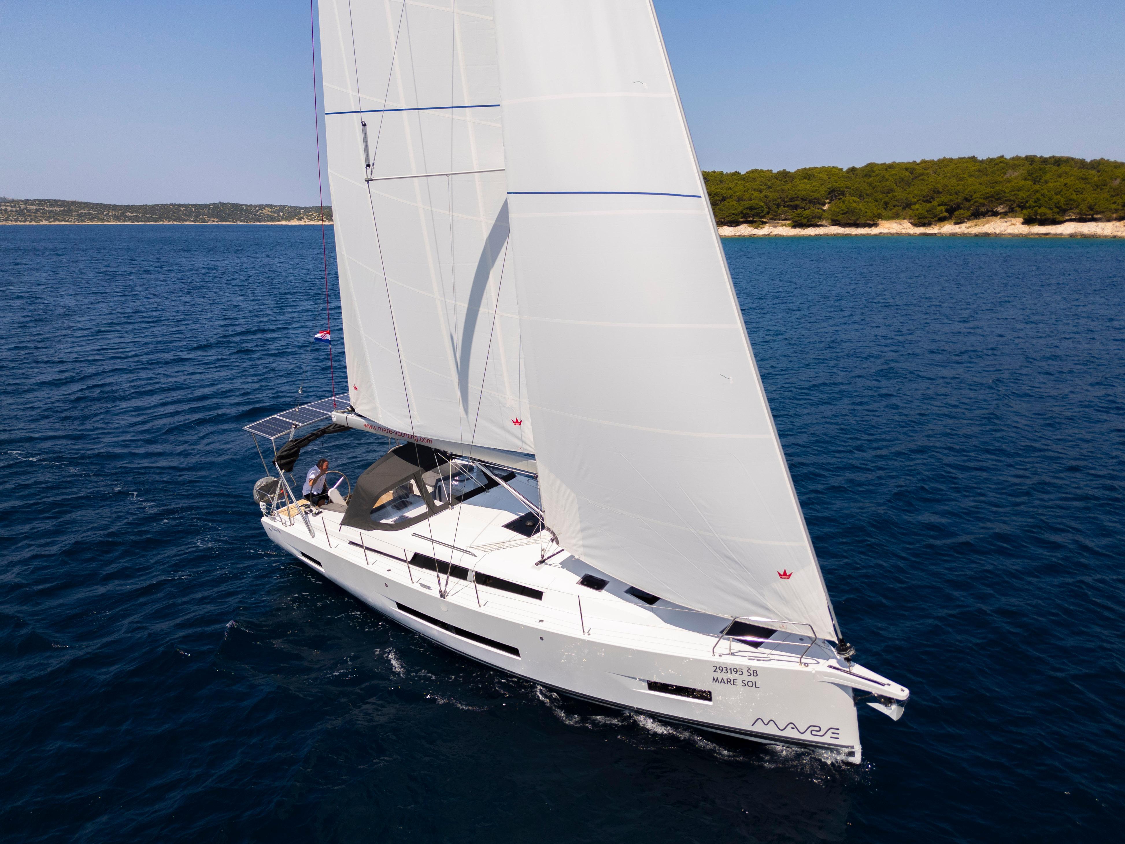Hanse 410 2025 Hanse 410 sailboat cruising on blue ocean near a forested coastline.