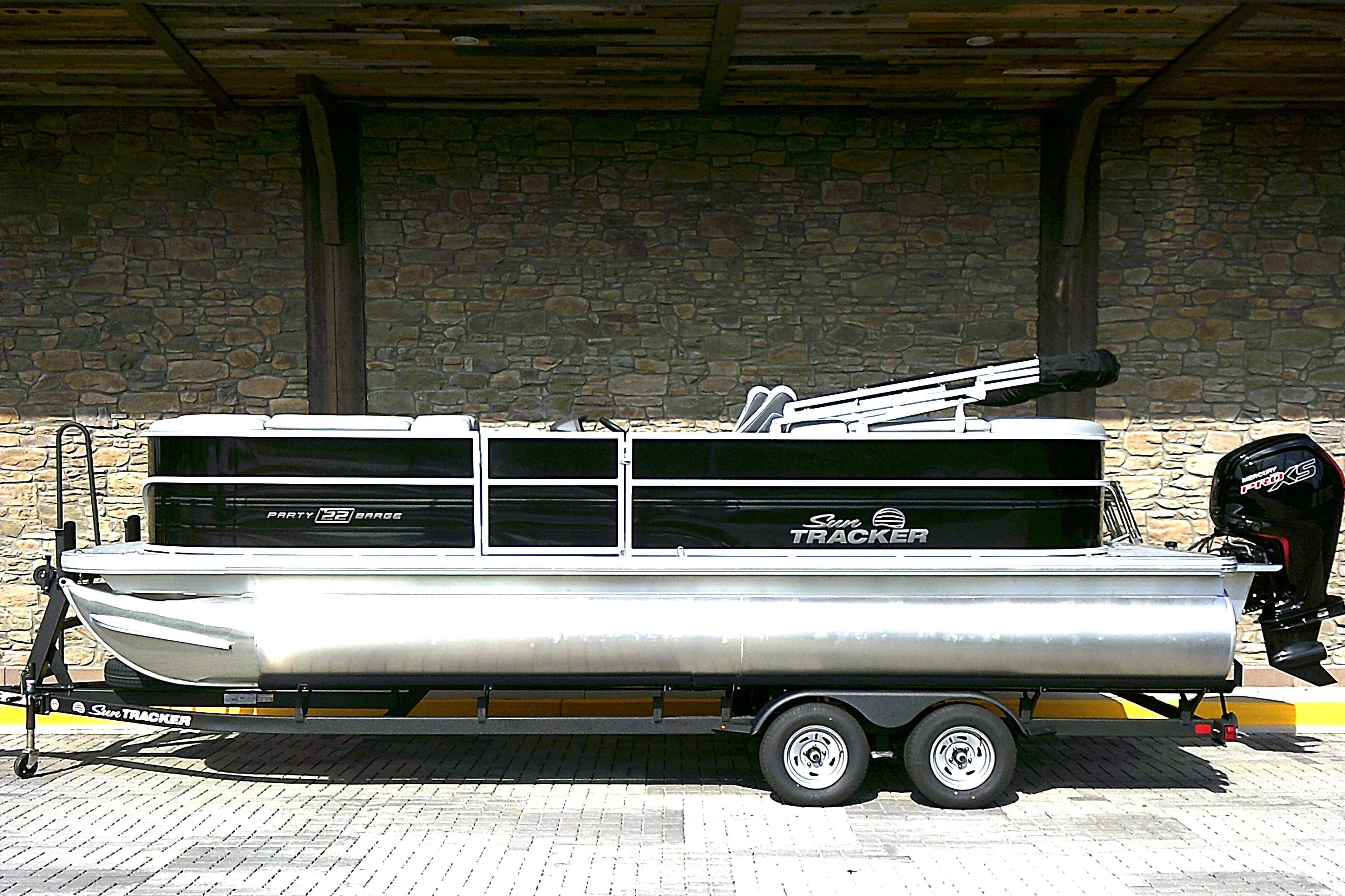 Sun Tracker Party Barge 22 DLX 2026 Sun Tracker Party Barge 22 DLX pontoon boat on trailer, parked by stone wall.