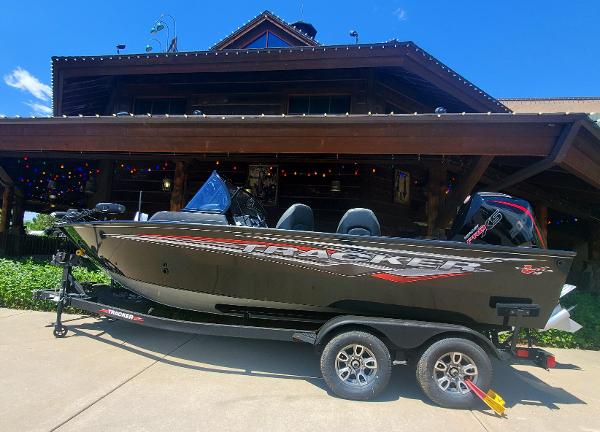 Tracker Targa V-19 WT 2024 Tracker Targa V-19 WT boat on trailer in front of a wooden house.