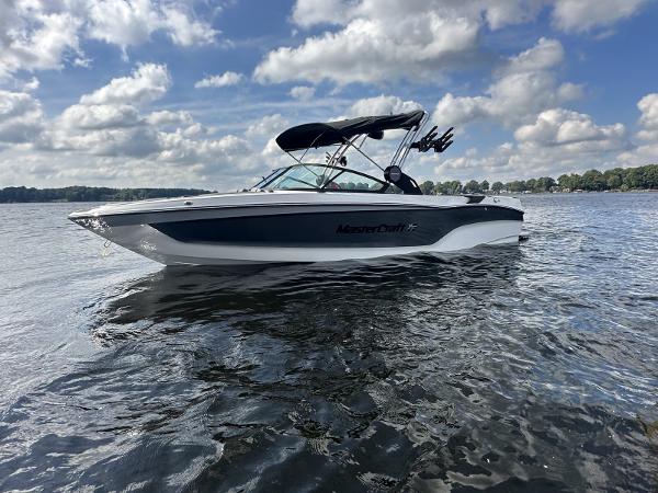 MasterCraft XT25 2024 MasterCraft XT25 boat on a lake under a cloudy sky.