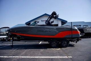 MasterCraft NXT22 2025 MasterCraft NXT22 boat in gray and red, parked on a trailer outside a dealership.