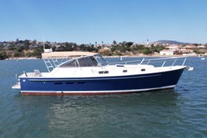 Legacy 40 1999 Legacy 40 boat with blue hull on calm water, scenic shoreline background.