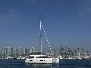Lagoon 42 2022 Lagoon 42 catamaran sailing near a marina with modern buildings and palm trees.