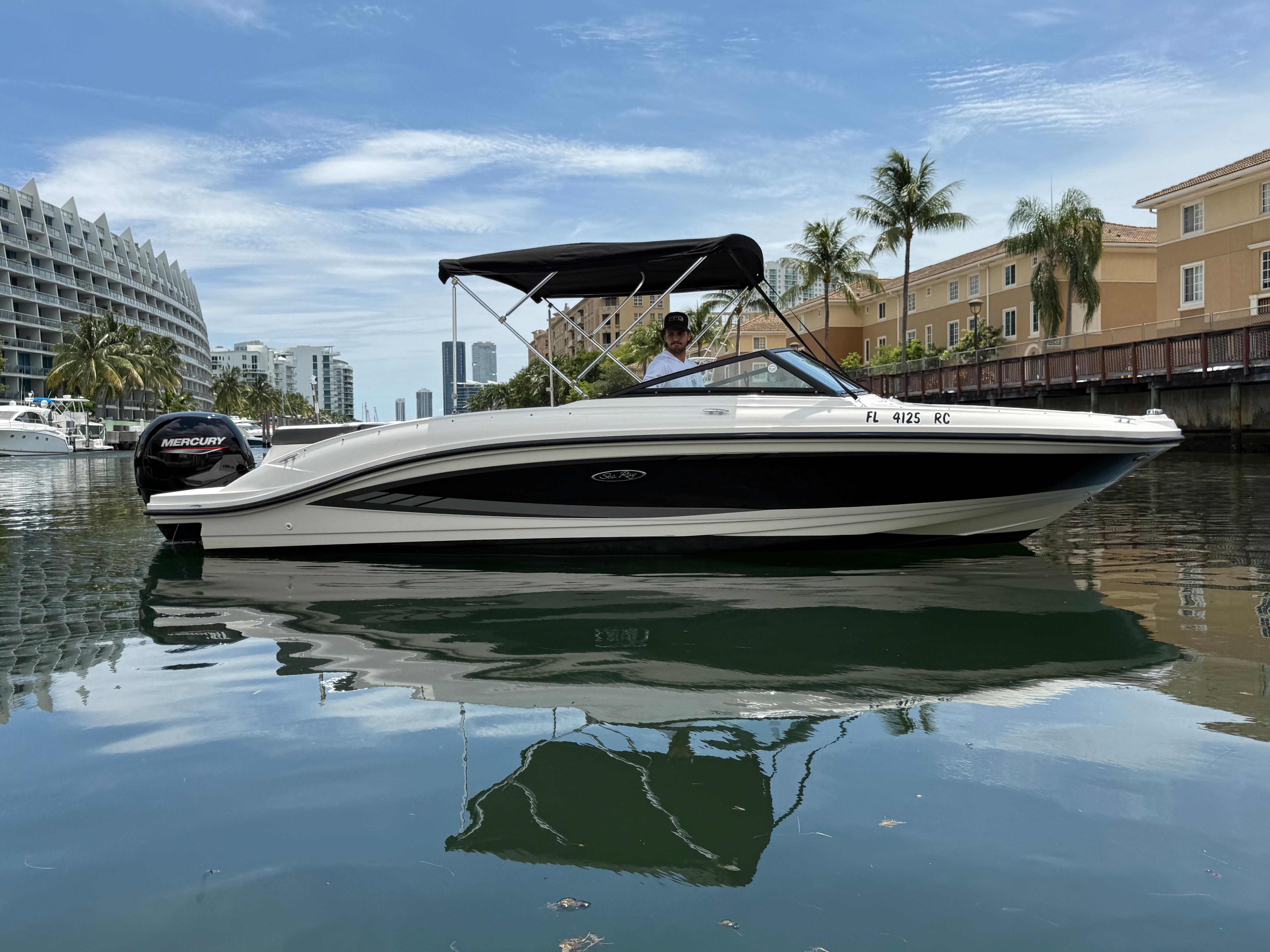 Sea Ray 21 SPX OB 2016 Sea Ray 21 SPX OB boat on calm water, with cityscape and palm trees in the background.