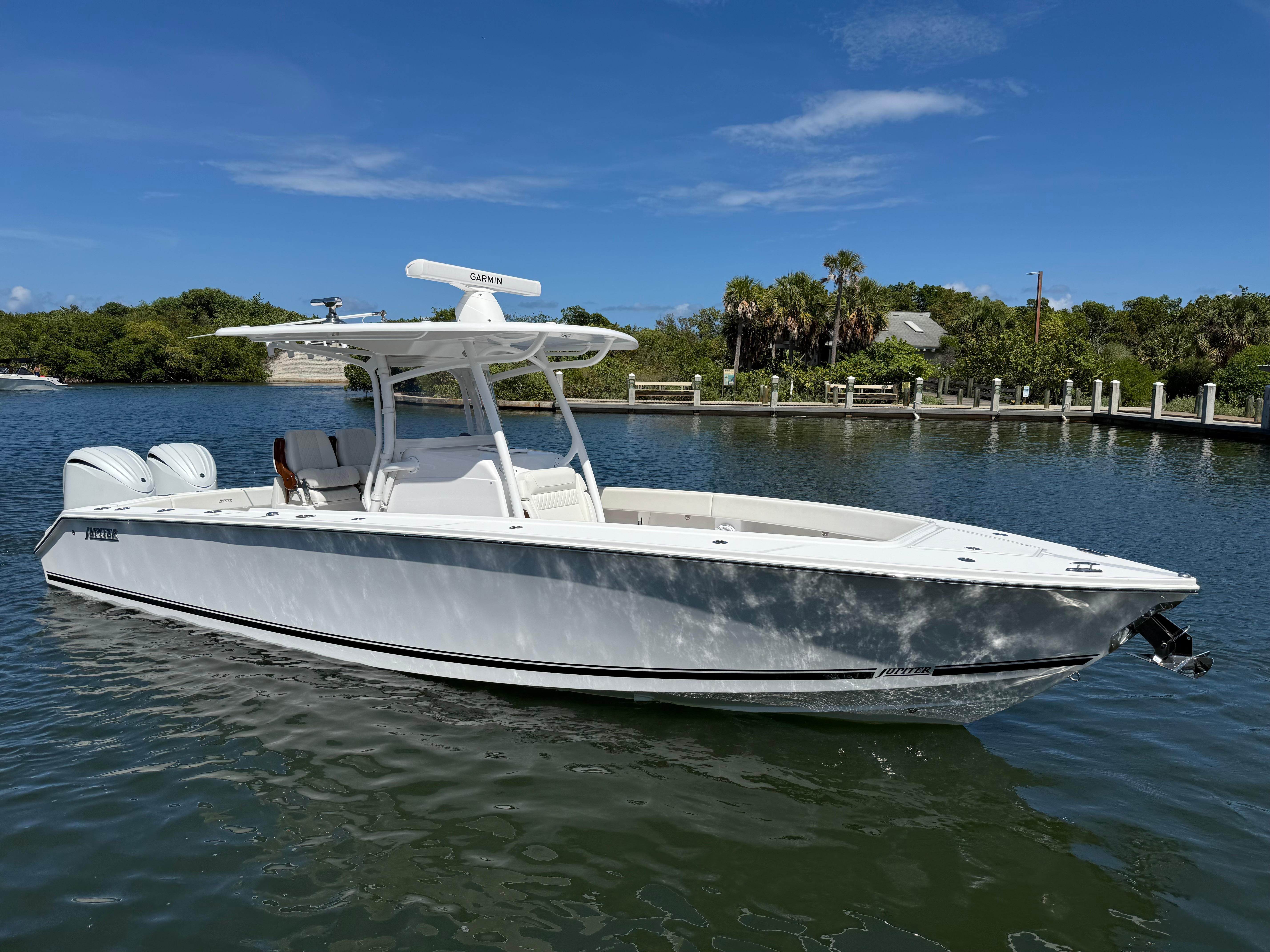 Jupiter 30 2023 Jupiter 30 boat on calm water, clear sky, lush greenery in background.