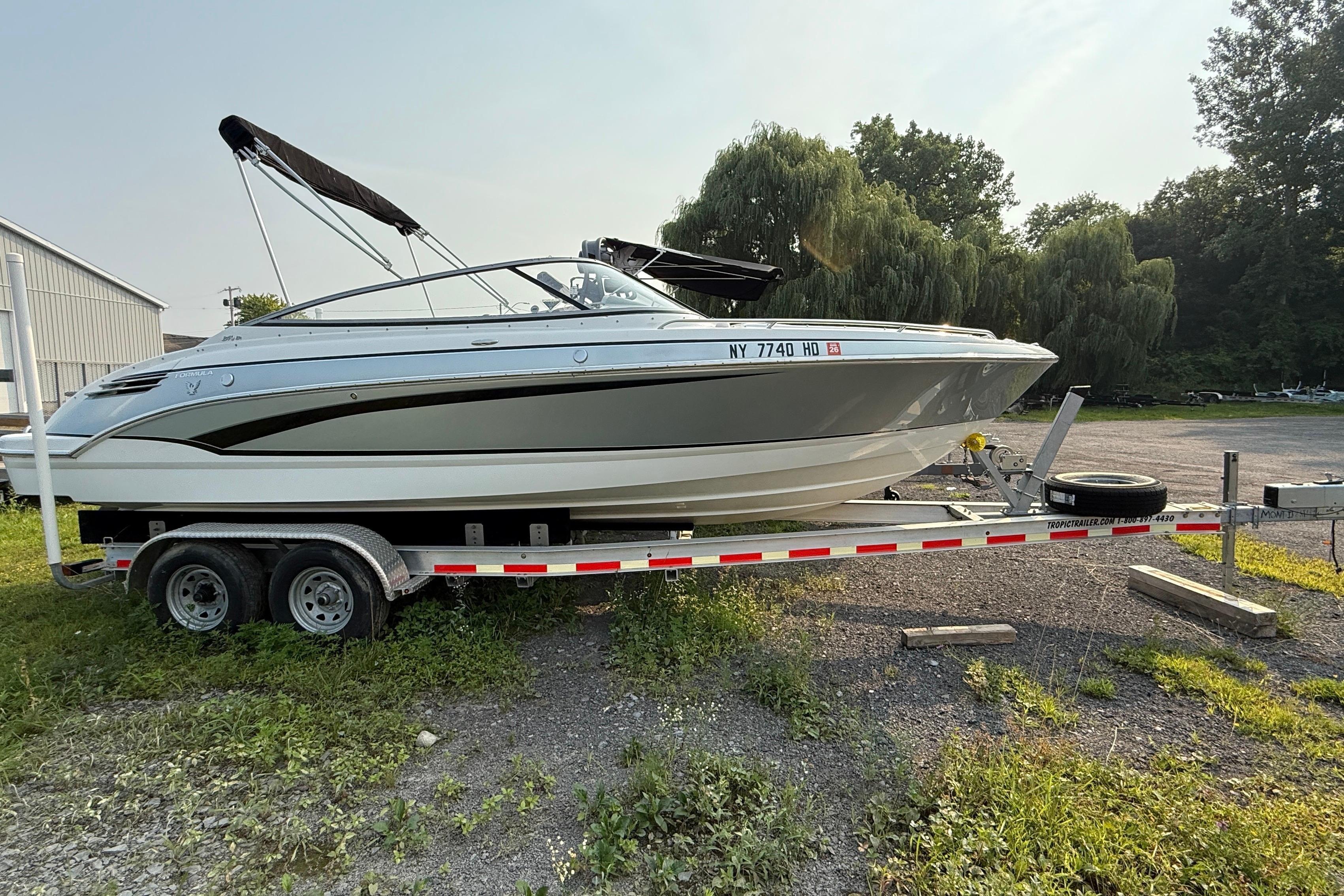 Formula 240 BR 2007 Formula 240 BR boat on trailer, parked outdoors with trees in the background.