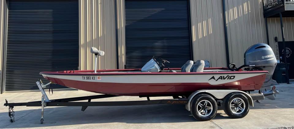 Avid 20 XB 2024 Avid 20 XB boat on trailer, red and white, parked outside a building.