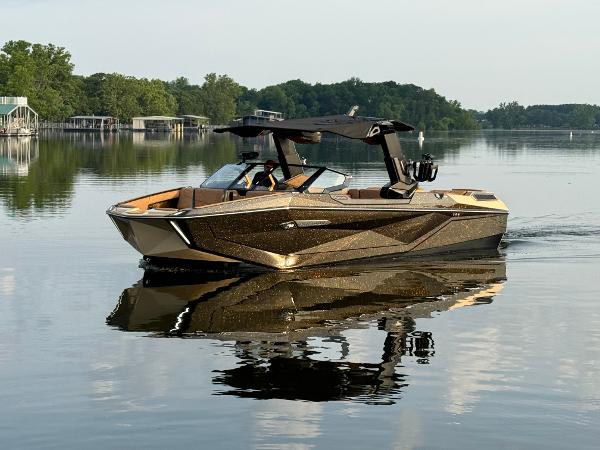 Nautique G25 Paragon 2025 Nautique G25 Paragon boat on calm lake with lush green shoreline.