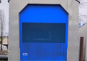 Custom Boathouse Custom 2017 boathouse with blue door, industrial setting, overcast sky.