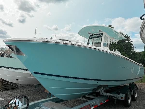 Cobia 285 Center Console 2025 Cobia 285 Center Console boat on trailer, light blue hull, cloudy sky background.