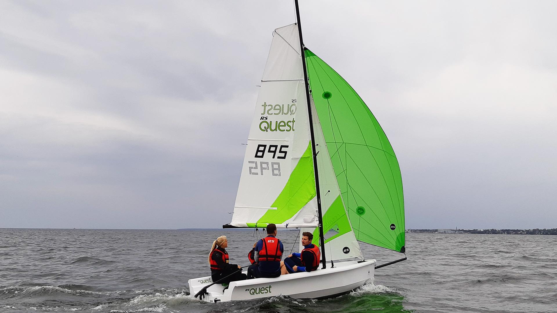 RS Quest 2024 RS Quest sailboat with green sail on open water, three people onboard.