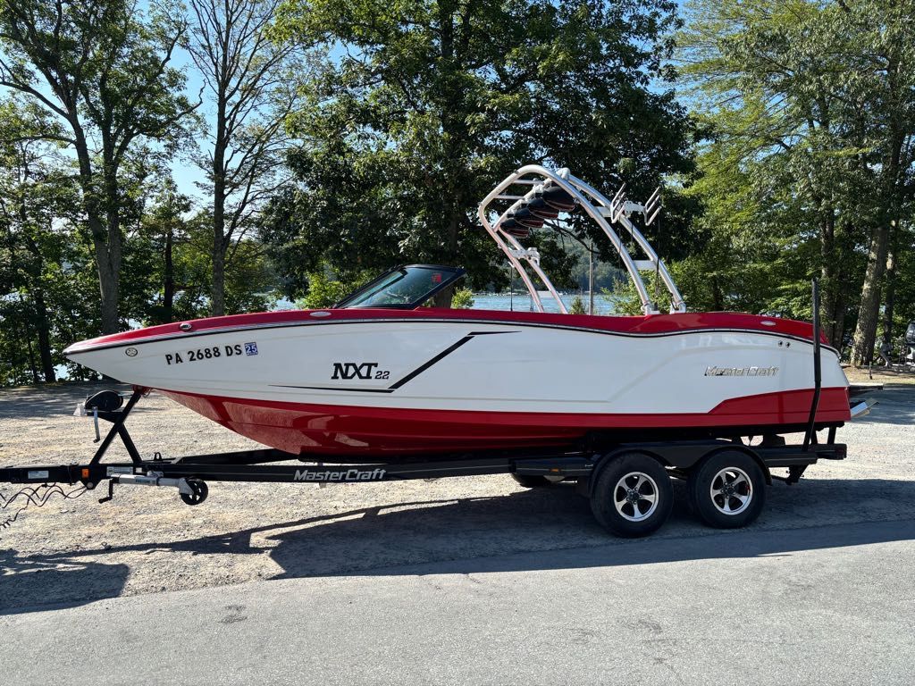 MasterCraft NXT22 2016 MasterCraft NXT22 boat on trailer, red and white, parked near trees.