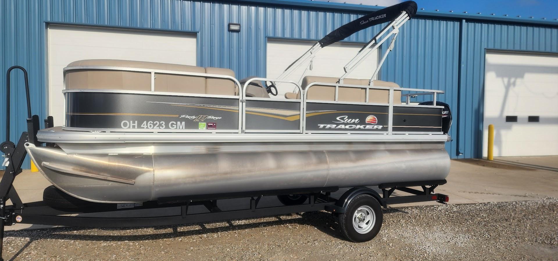 Sun Tracker Party Barge 18 DLX 2024 Sun Tracker Party Barge 18 DLX pontoon boat on trailer, parked outside blue building.