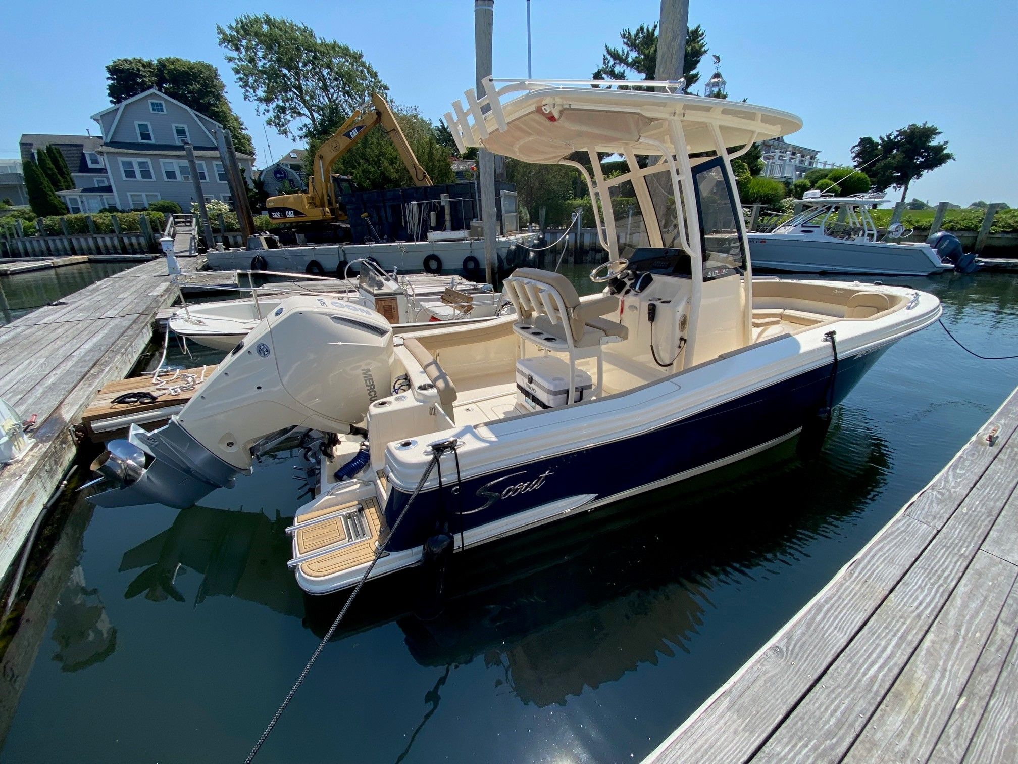 Scout 215XSF 2025 Scout 215XSF boat docked in a marina, featuring a sleek design and powerful outboard motor.