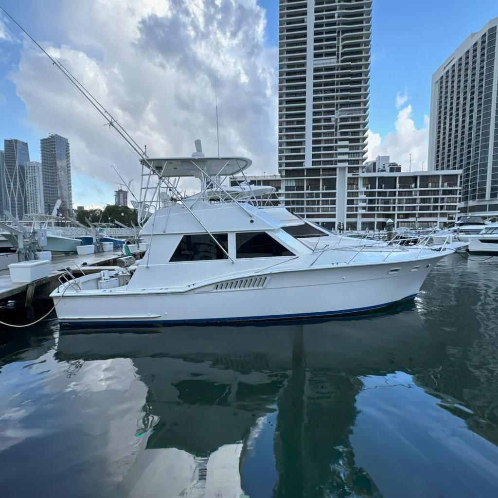 Hatteras Convertible 1982 Hatteras Convertible yacht docked in a marina with city skyline backdrop.