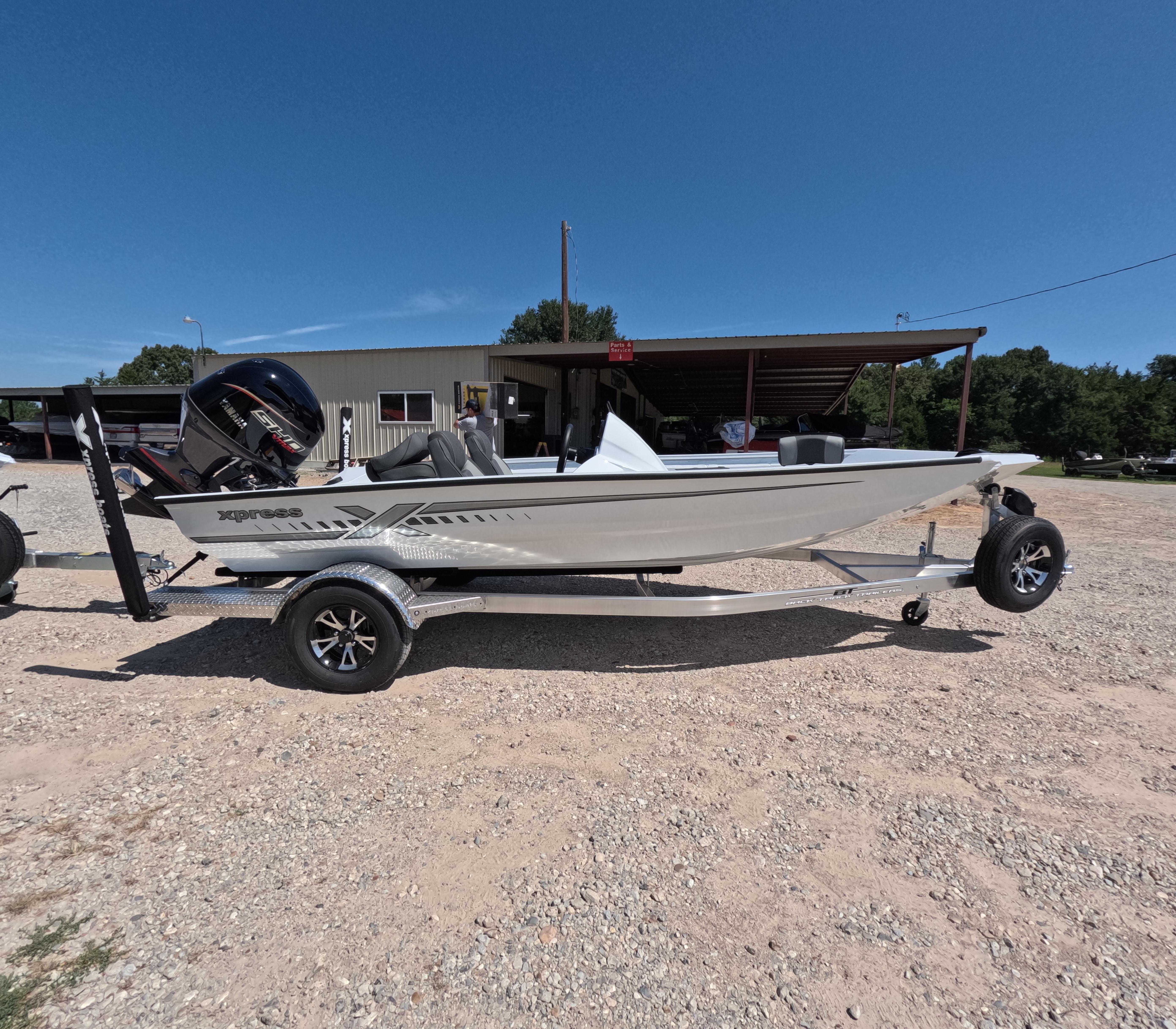 Xpress H 18 BASS 2026 Xpress H 18 BASS boat on trailer, parked outdoors under clear blue sky.