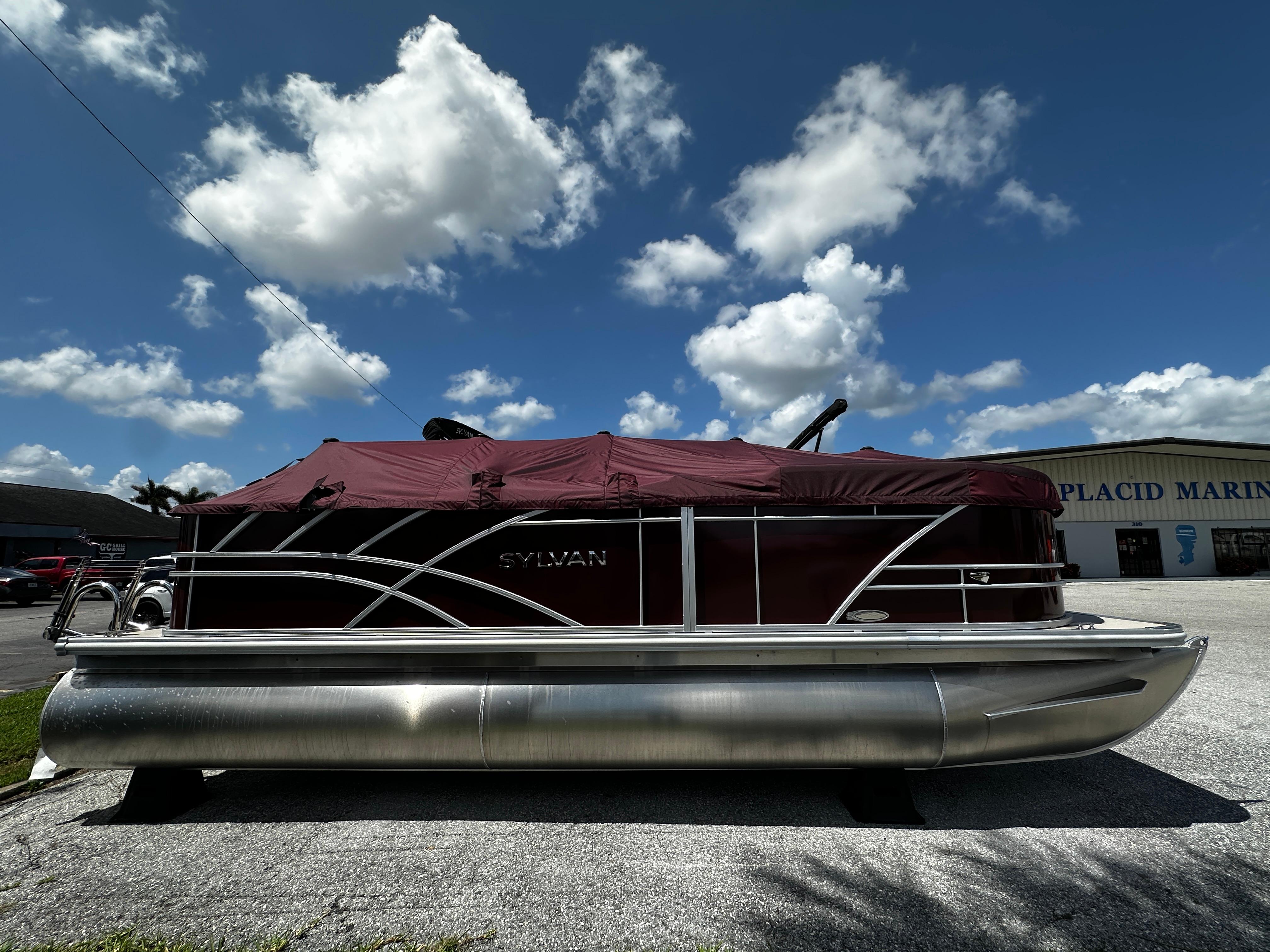 Sylvan Mirage 820 Cruise 2025 Sylvan Mirage 820 Cruise pontoon boat with maroon cover, parked outdoors under blue sky.