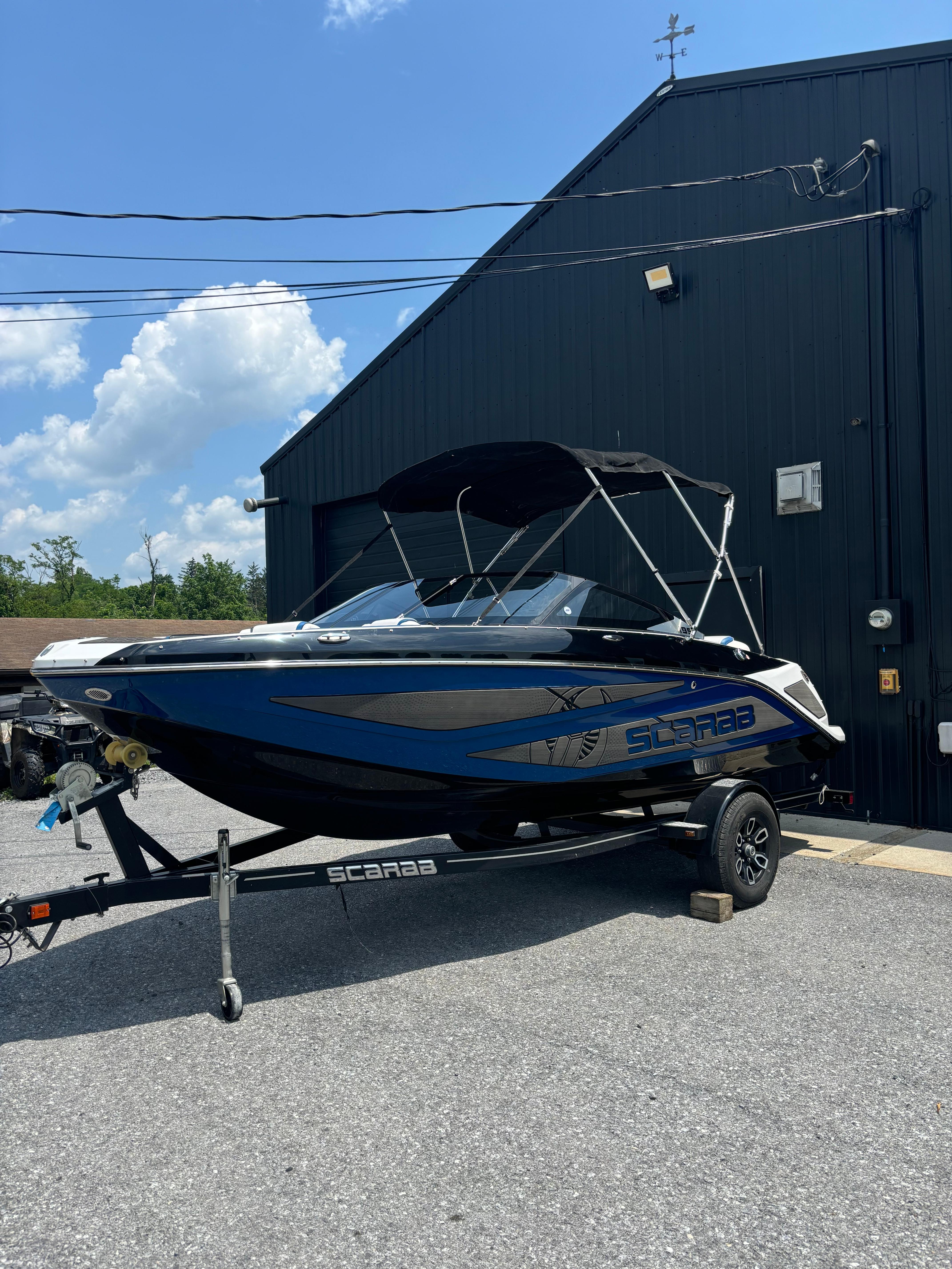 Scarab 195 H.O. 2025 Scarab 195 H.O. boat on trailer, parked outdoors near a black building.