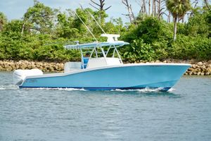 Invincible 36 CC Blue Invincible boat cruising on water near lush green shoreline.
