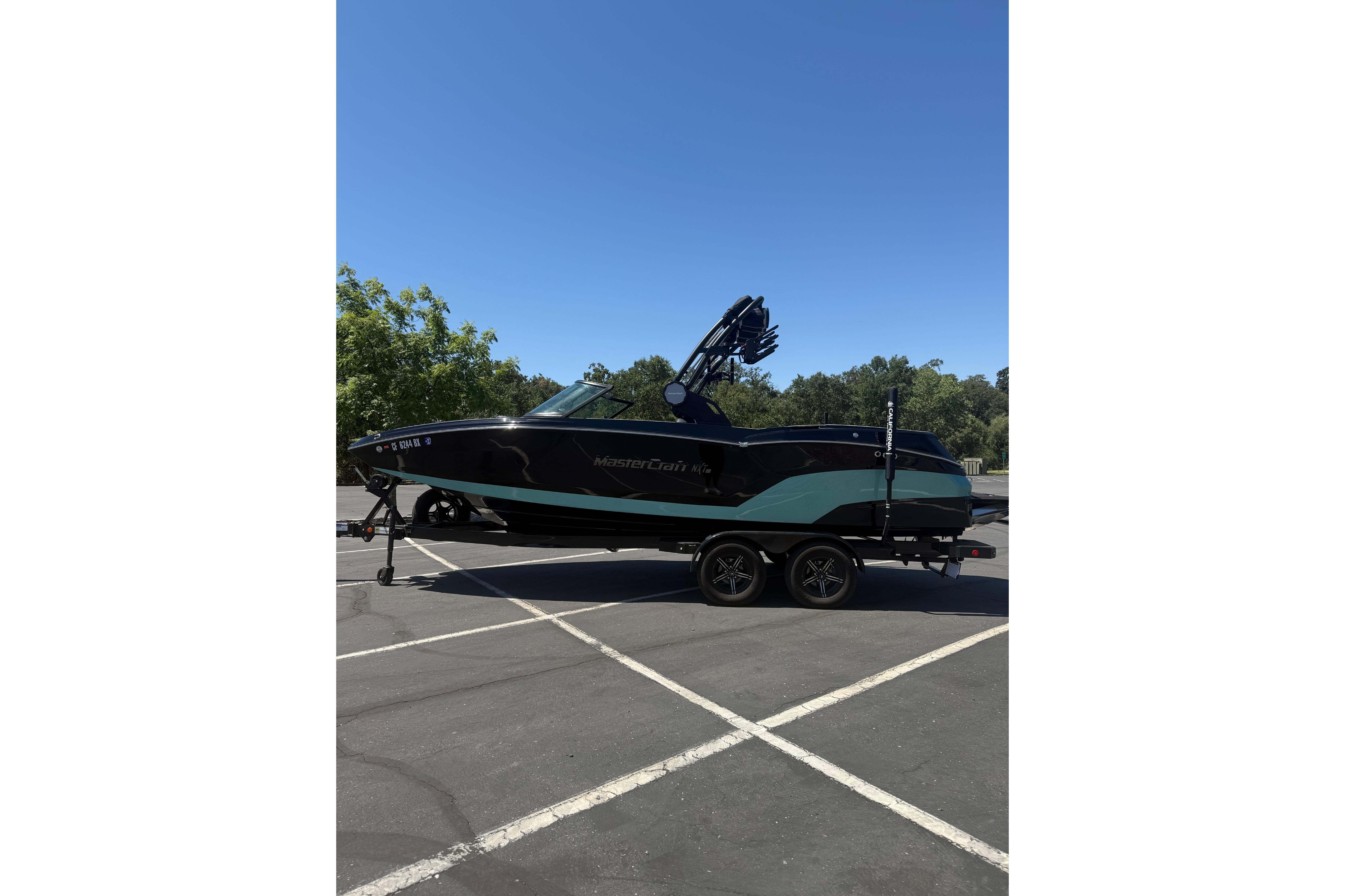 MasterCraft NXT22 2025 MasterCraft NXT22 boat on trailer in parking lot under clear blue sky.