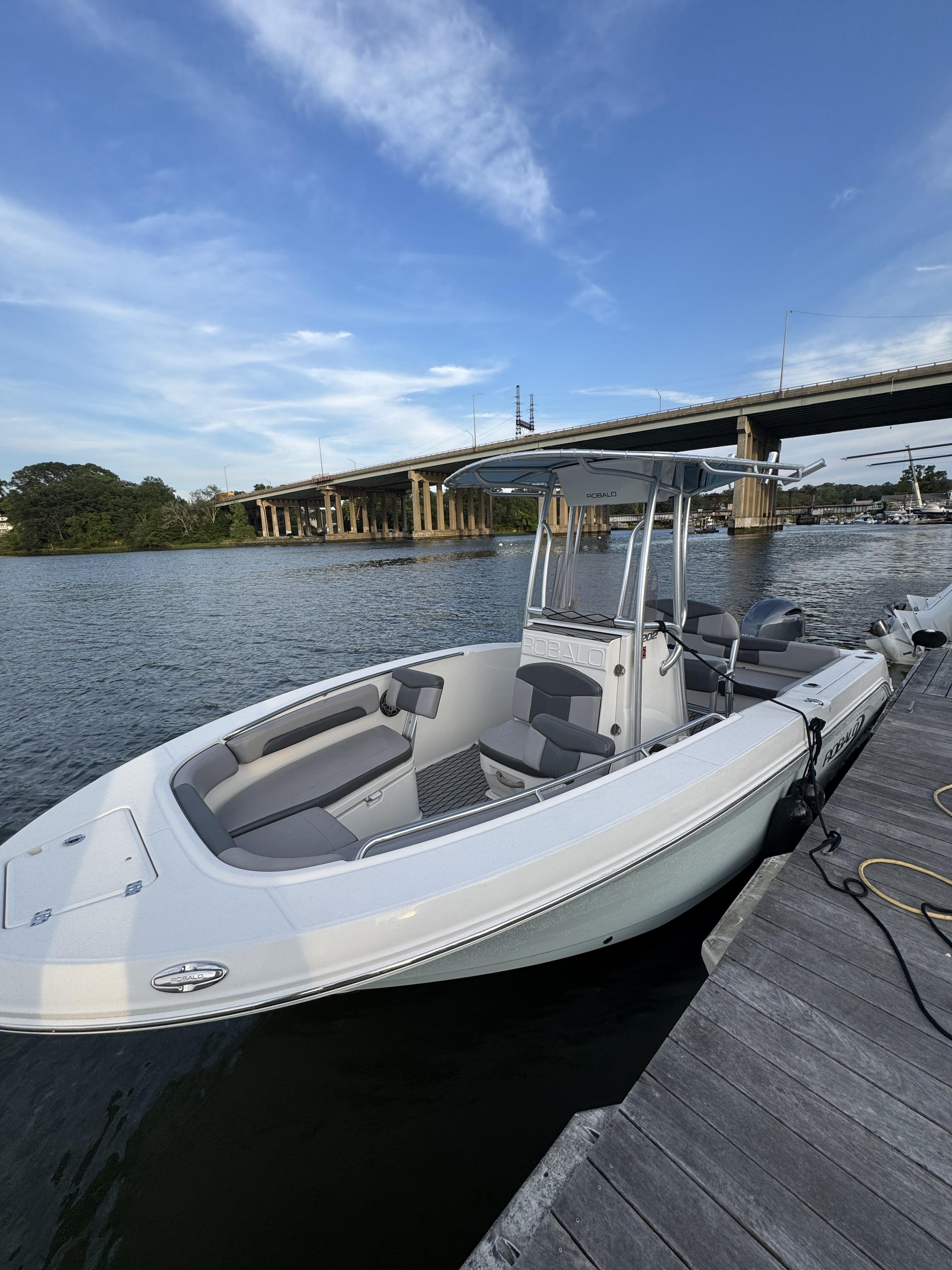 Robalo R202 Explorer 2019 Robalo R202 Explorer boat docked by a scenic river under a bridge.