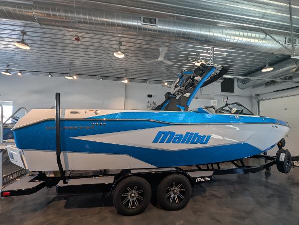 Malibu Wakesetter 25 LSV 2025 Malibu Wakesetter 25 LSV boat in showroom, blue and white design, on trailer.