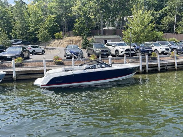 Cobalt CS23 2024 Cobalt CS23 boat docked by a lakeside parking area with cars and trees.