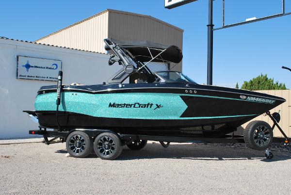 MasterCraft XStar 2022 MasterCraft XStar boat on trailer, turquoise and black design, parked outdoors.
