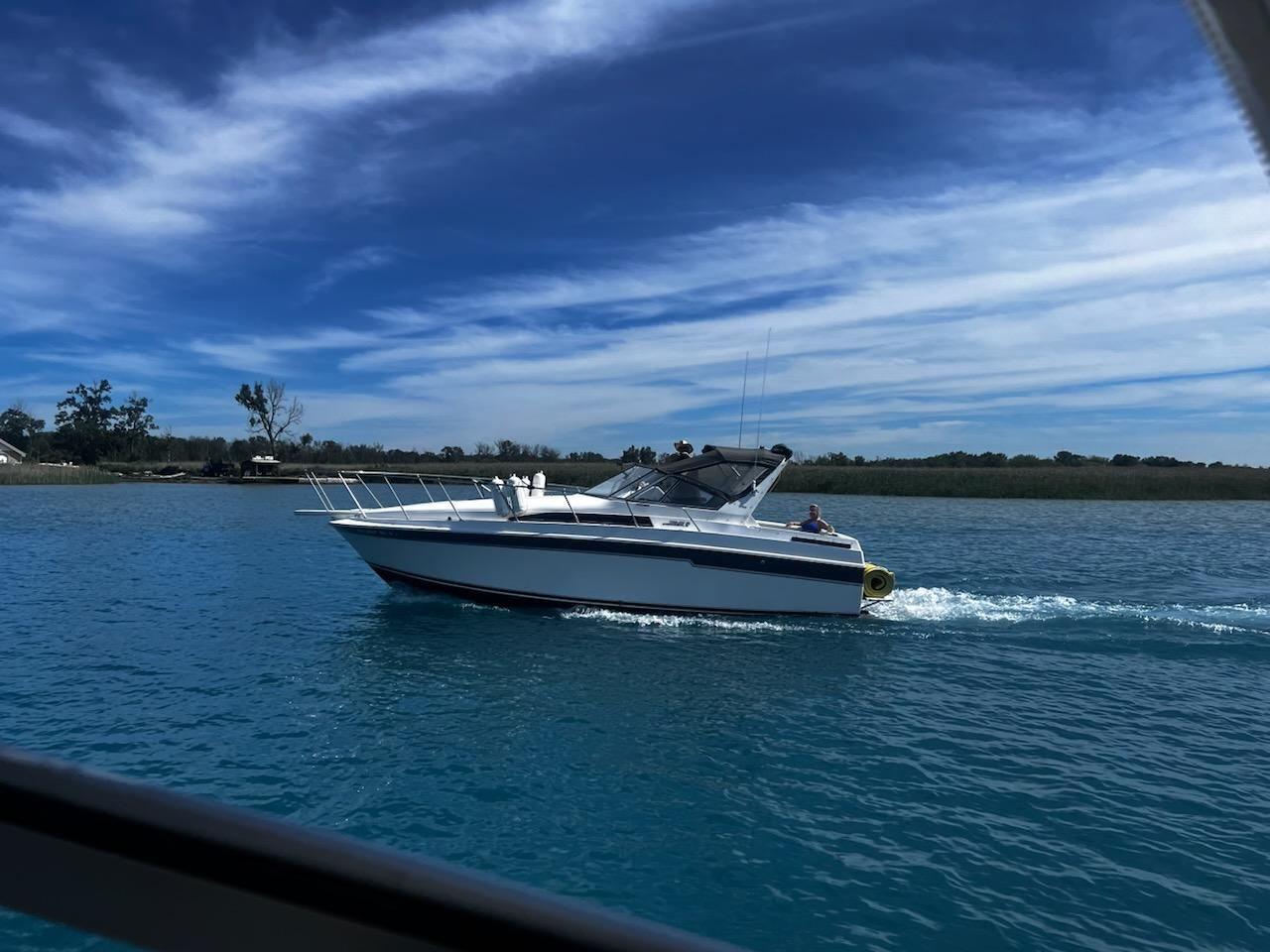 Trojan 10.8 Meter International 1988 Trojan International boat cruising on a clear blue lake under a vibrant sky.