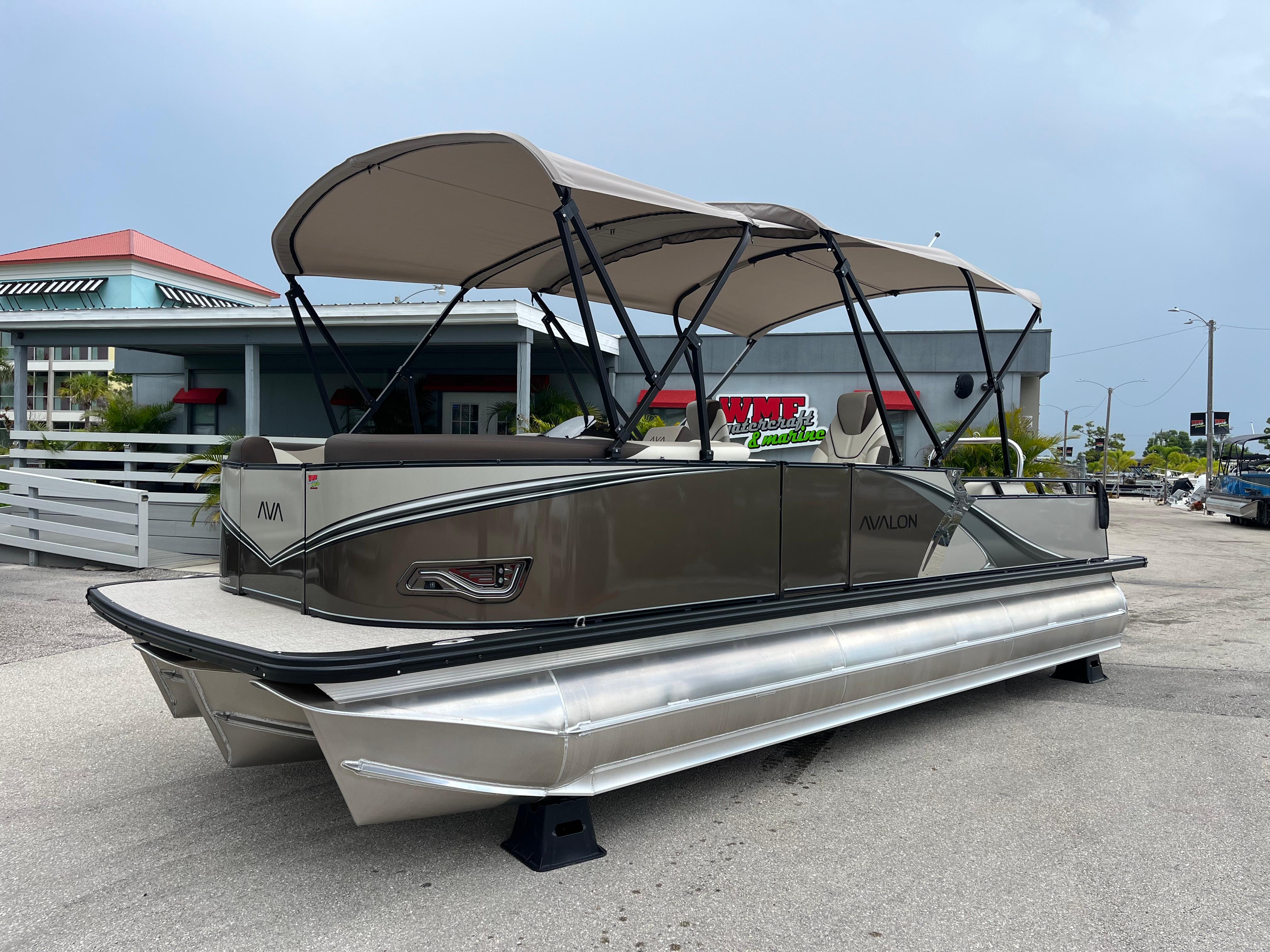 Avalon 2385 LSZ Versatile Rear Bench, Tri Toon High Performance 2026 Avalon 2385 LSZ Versatile Rear Bench Tri Toon boat with canopy, parked outdoors.