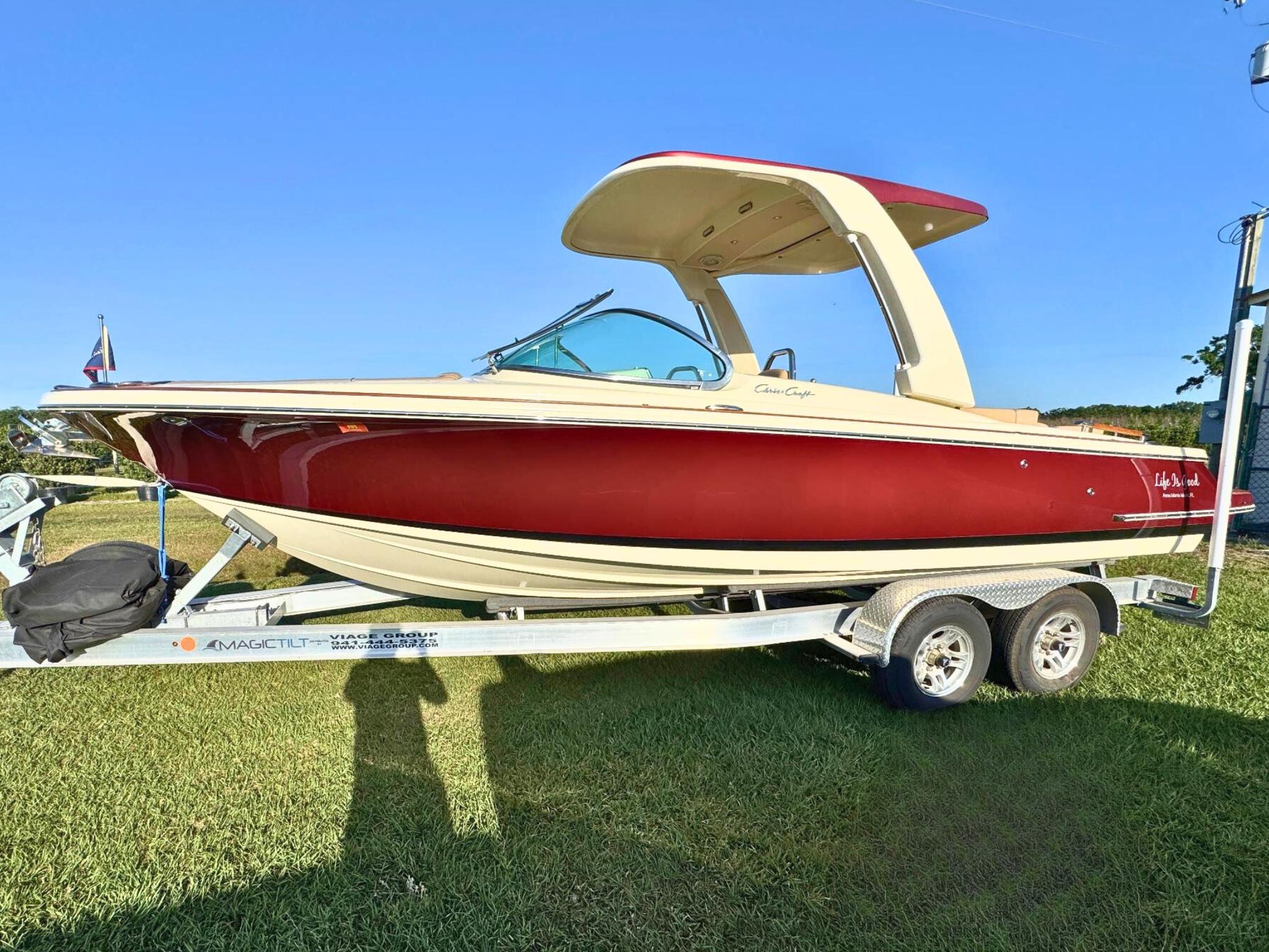 Chris-Craft Launch 25 GT 2022 Chris-Craft Launch 25 GT boat on trailer, red and cream design, sunny day.