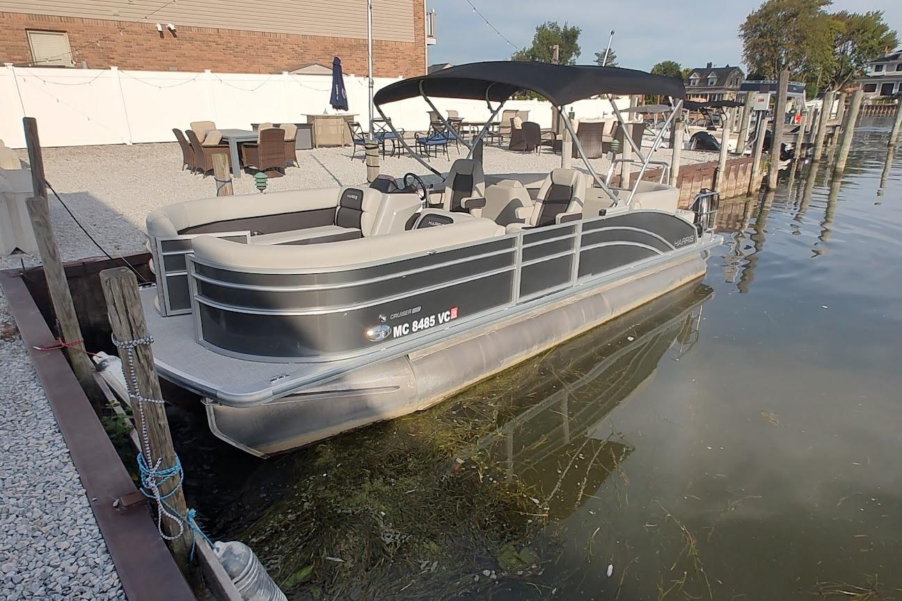 Harris Cruiser 230 2024 Harris Cruiser 230 pontoon boat docked by a waterfront patio.